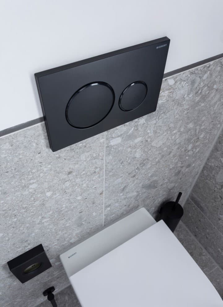 Czarny przycisk spłukujący Geberit Sigma20 zamontowany na ścianie nad wiszącą miską WC z zabudowanym stelażem podtynkowym Czarny przycisk spłukujący Geberit Sigma20 zamontowany na ścianie nad wiszącą miską WC z zabudowanym stelażem podtynkowym