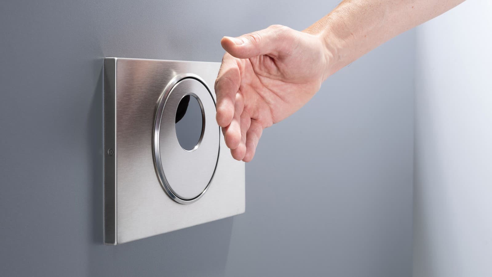 Dłoń zbliżona do bezdotykowego przycisku spłukującego Geberit Sigma10 okrągłego z funkcją zdalnego spłukiwania Dłoń zbliżona do bezdotykowego przycisku spłukującego Geberit Sigma10 okrągłego z funkcją zdalnego spłukiwania